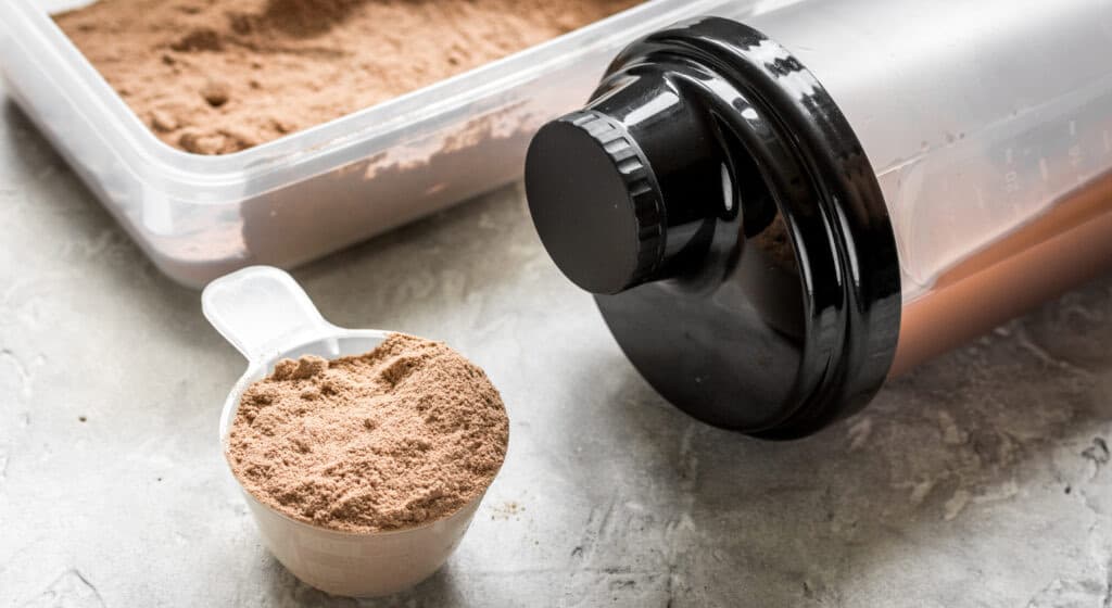 A scoop of chocolate protein powder beside a shaker bottle