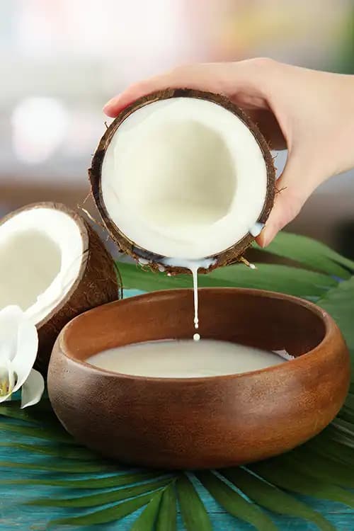 Coconut milk pouring from a cracked coconut into a wooden bowl