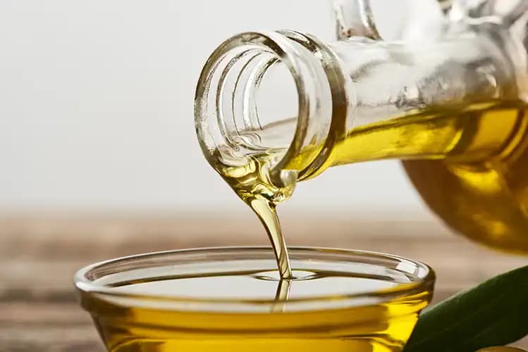 Golden oil pouring from a bottle into a glass bowl